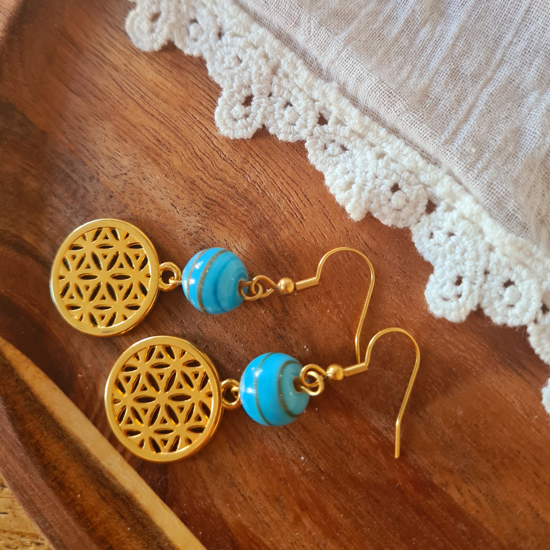 One of a kind oorbellen met blauwe glaskraal en goudkleurige bedel