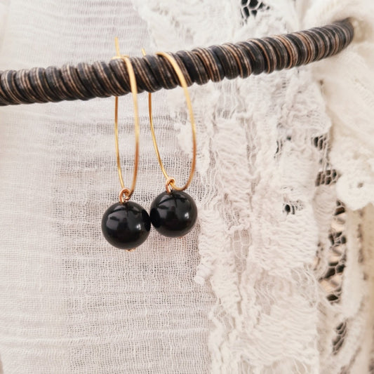 Goudkleurige ringetjes met zwarte obsidiaan kraal hangend aan display, detail van natuursteen oorbellen met gouden ringen