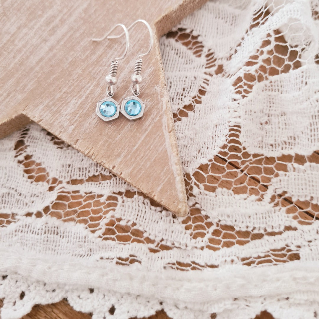 Zilveren oorbellen met lichtblauwe geboortesteen maart op kant met houten achtergrond, elegante geboortesteen oorbellen