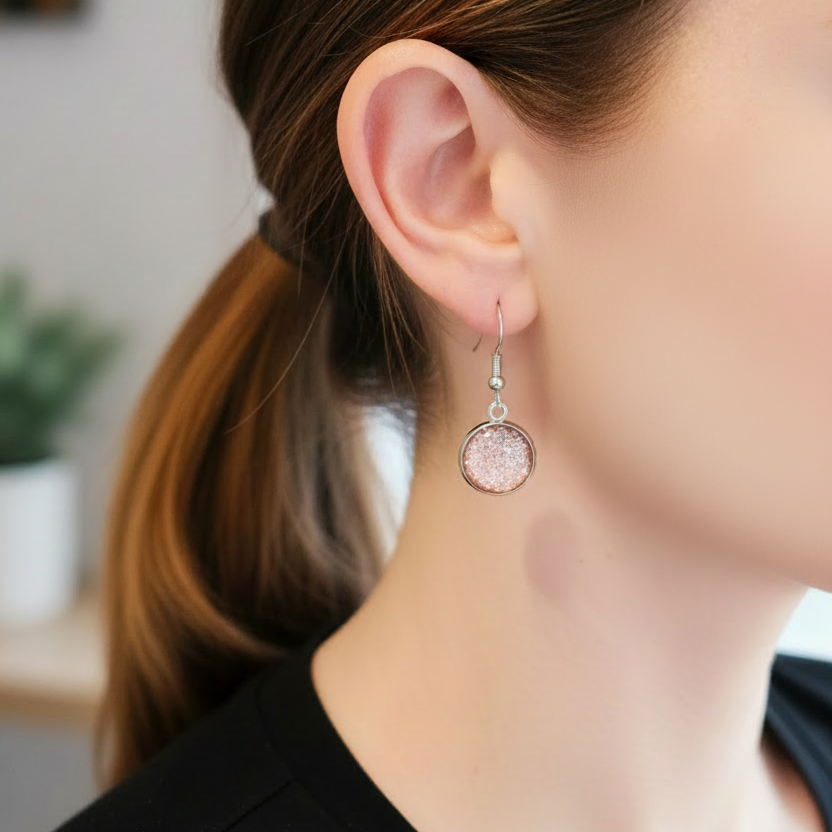 Gedragen zilverkleurige oorbellen met roze glittersteentje, korte hangertjes met oorhaakje