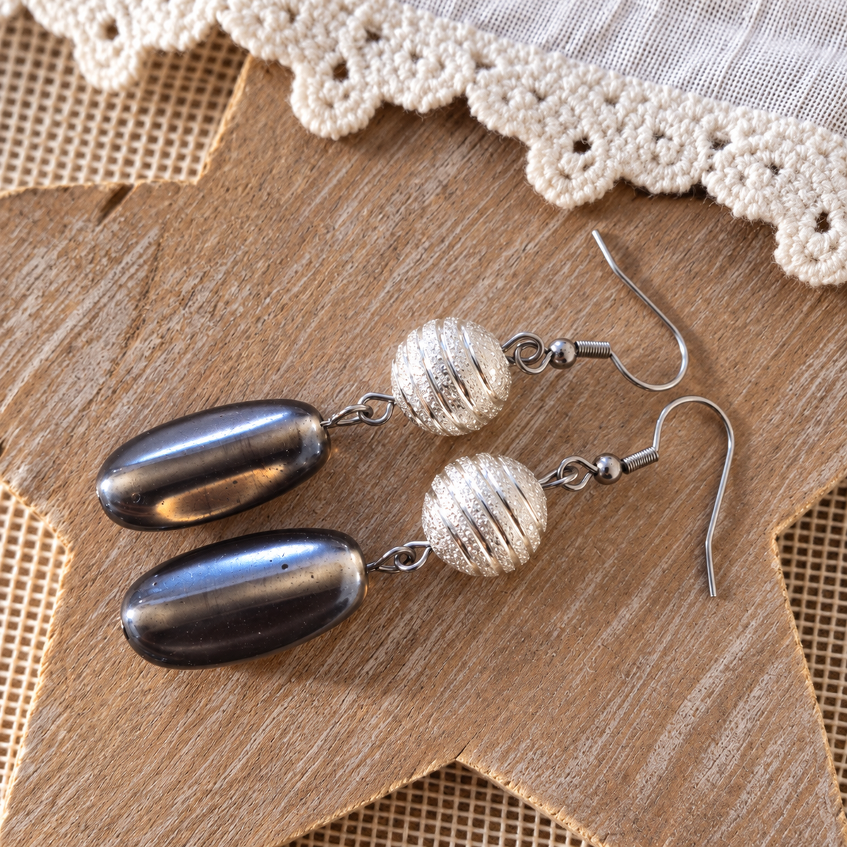 Handgemaakte limited edition oorbellen met ovale antracietkleurige glaskralen en ronde geribbelde zilverkleurige metalen bolletjes