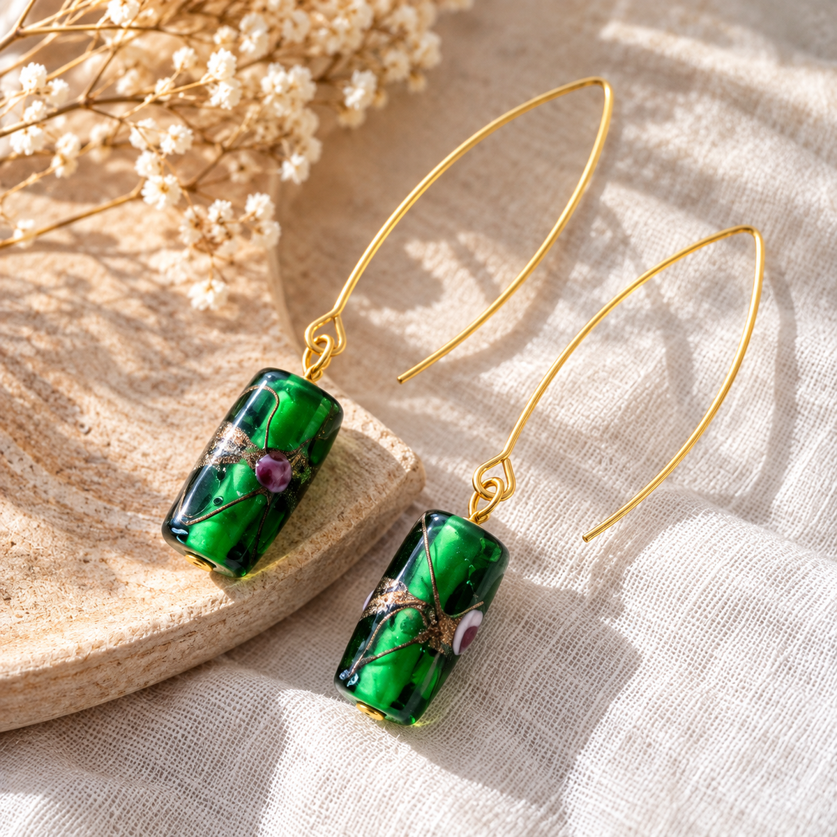 Limited edition oorbellen met cilindervormige groene glaskraal en een patroon van donkere en goudkleurige lijnen met roze details