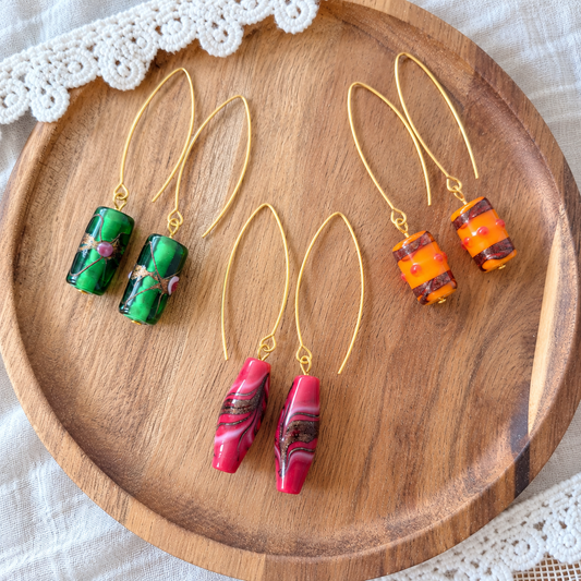 Limited edition oorbellen met glaskraal in groen met roze details, oranje met donkere banen en rood met golvende donkere strepen
