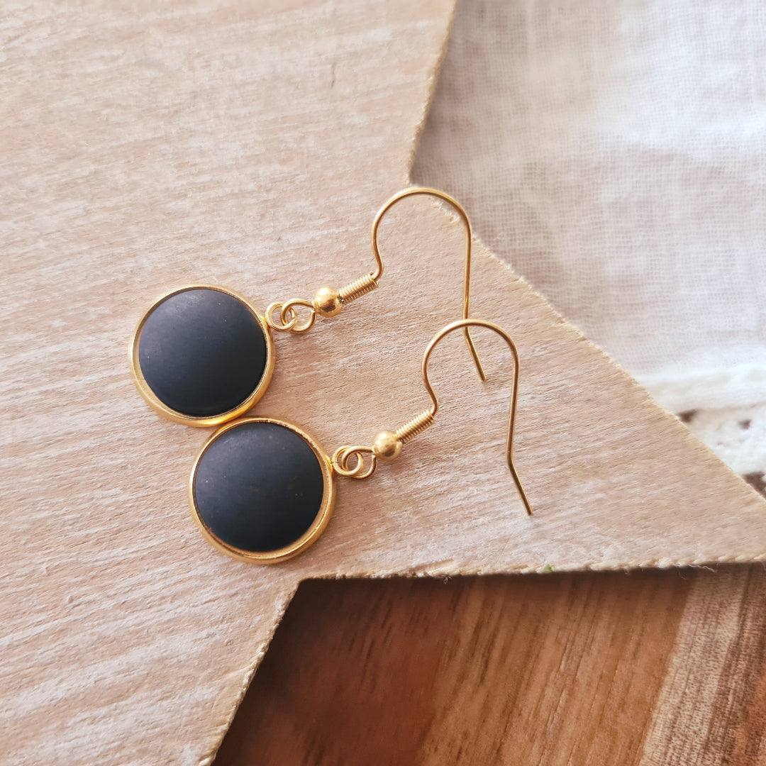 Korte oorbellen met matzwarte steen in zilver en goud op witte achtergrond