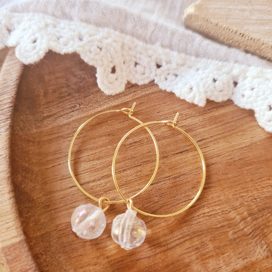 Gouden stainless steel ringen met transparante glaskraal uit India op houten ondergrond, minimalistische oorbellen