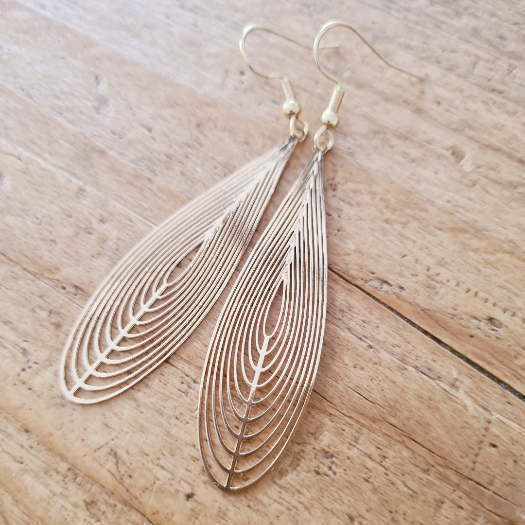 Goudkleurige druppelvormige filigraan oorbellen met opengewerkt patroon op witte kanten ondergrond, elegante lange oorbellen voor vrouwen