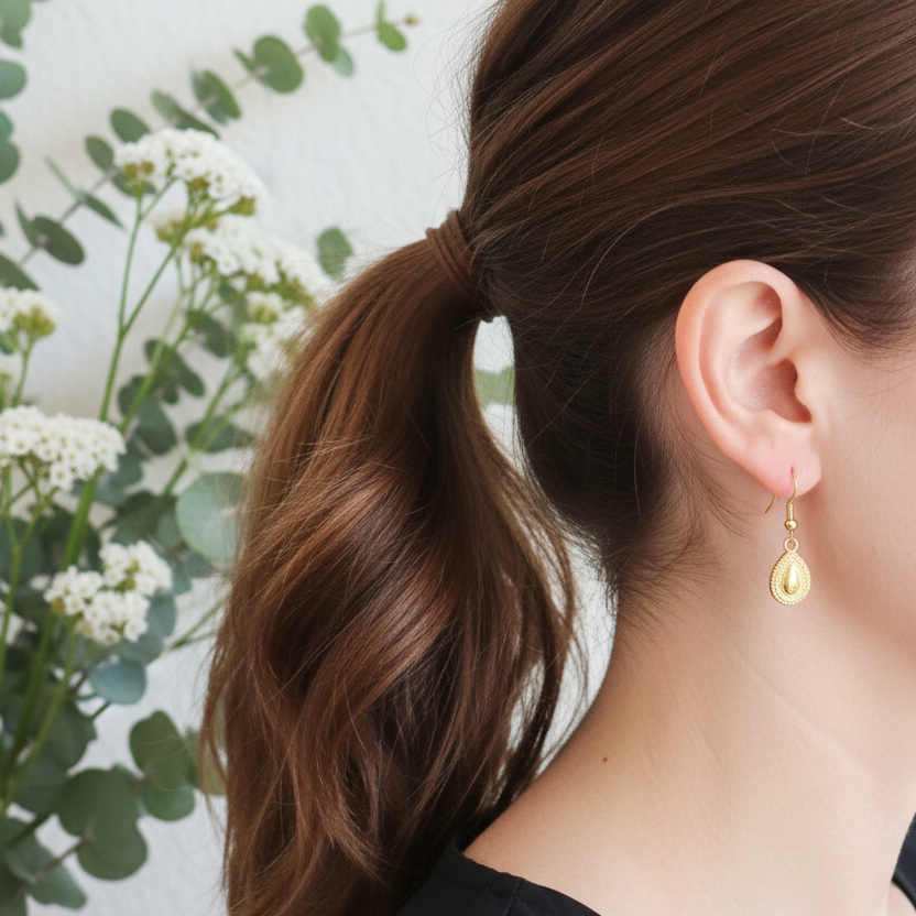 Detailfoto goudkleurige druppel oorbellen met subtiel bewerkte rand, tijdloos elegant design
