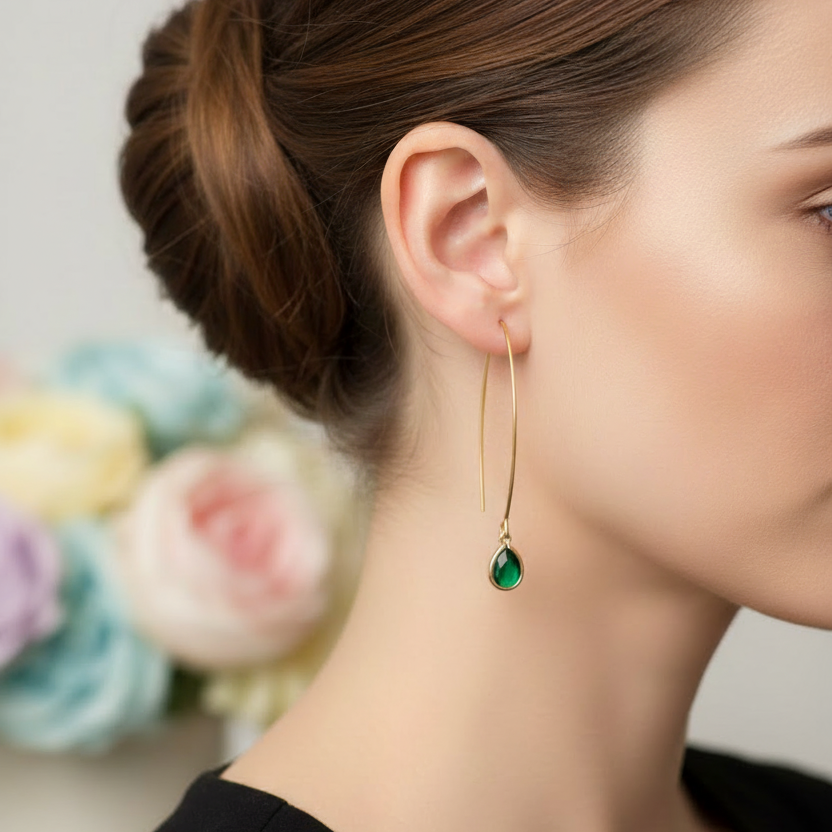 Goudkleurige oorbellen met groene druppelsteen gedragen door model, close-up profiel