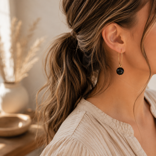 Model draagt goudkleurige ringetjes met zwarte obsidiaan kraal, elegante minimalistische oorbellen met natuursteen gedragen