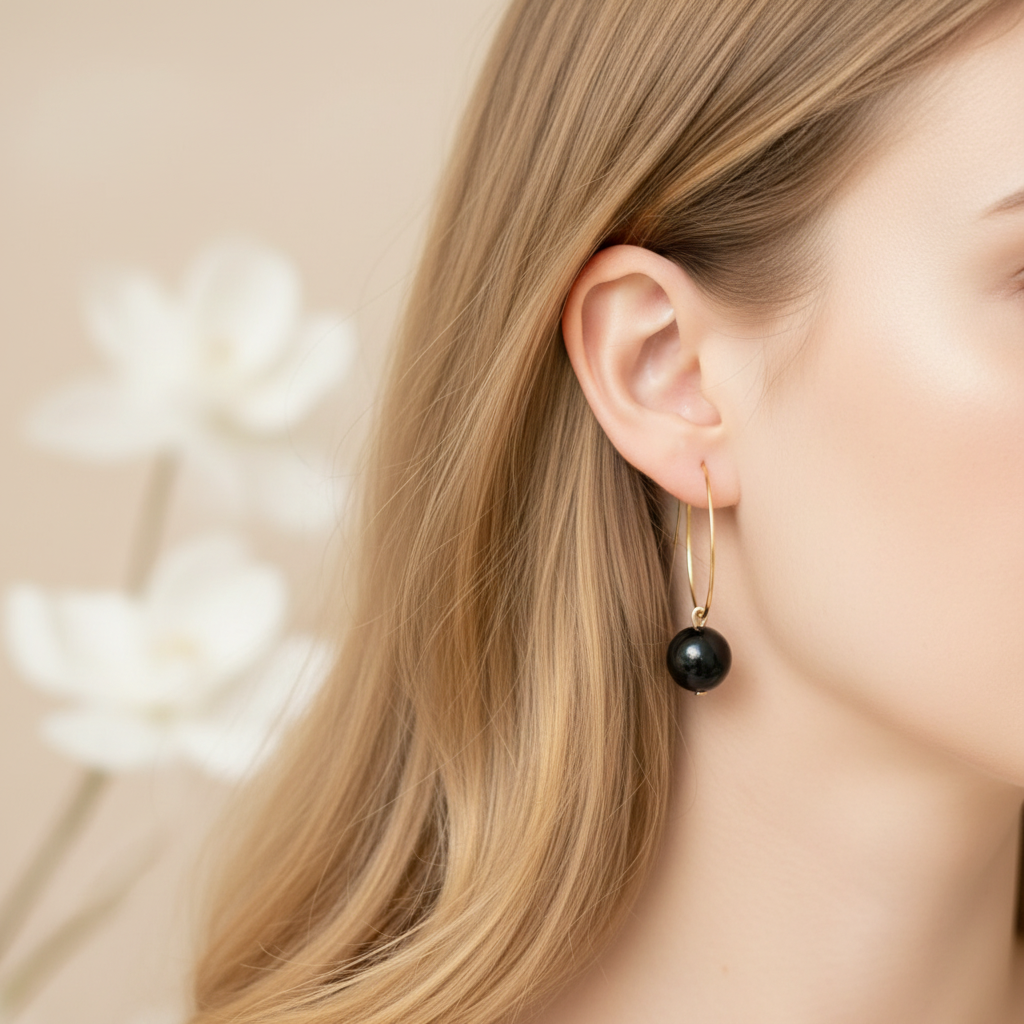 Model draagt goudkleurige ringetjes met zwarte obsidiaan kraal, elegante minimalistische oorbellen met natuursteen gedragen