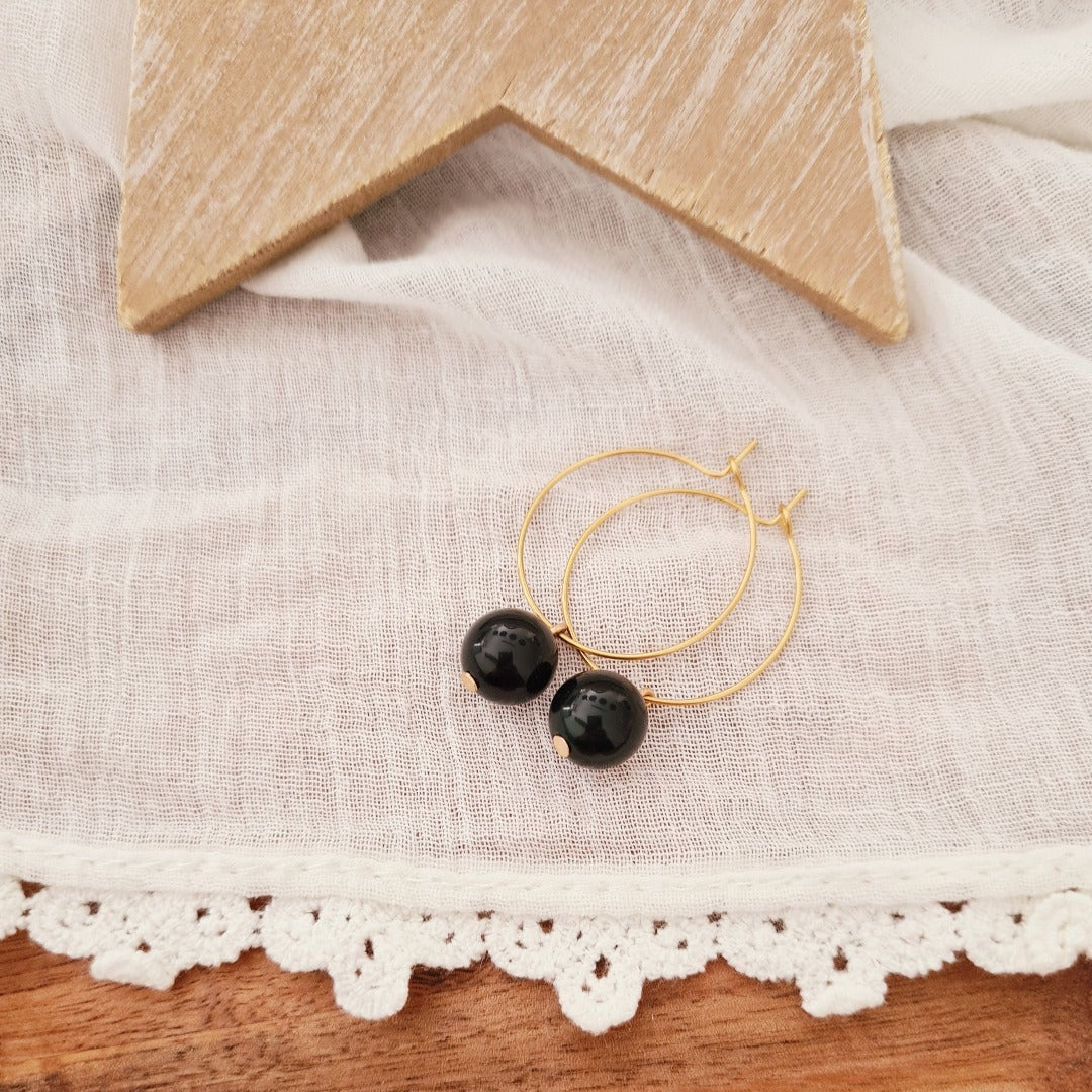 Goudkleurige ringetjes met zwarte obsidiaan kraal op witte ondergrond, elegante minimalistische oorbellen met natuursteen