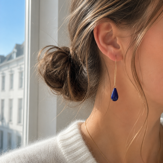 Lange goudkleurige oorbellen met blauwe Polaris Elements druppel gedragen aan oor