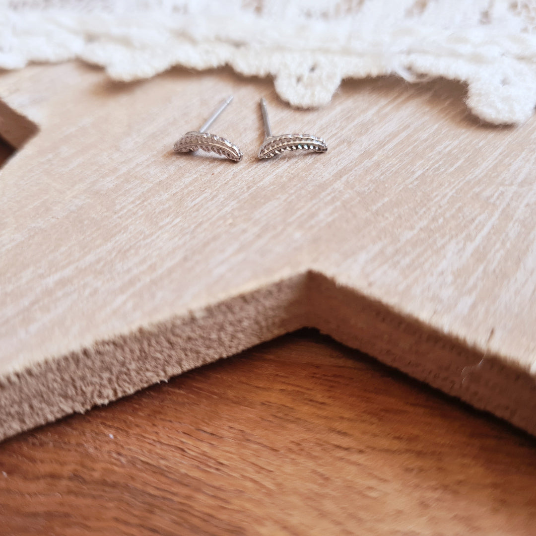 Zilverkleurige stekertjes met subtiel veertje op houten ondergrond