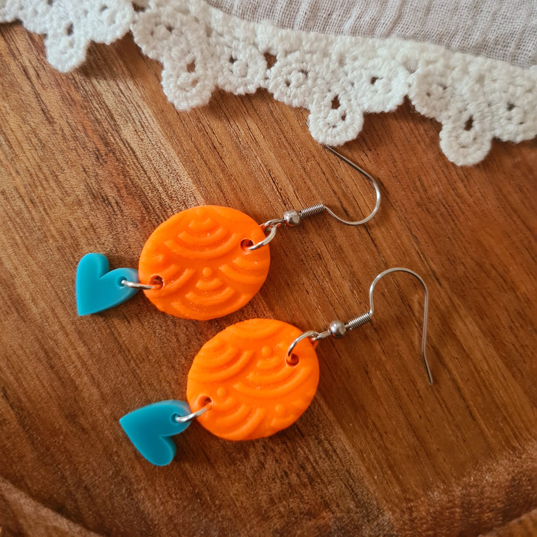 Handgemaakte polymeerklei oorbellen met oranje reliëfbedel en blauw plex hartje