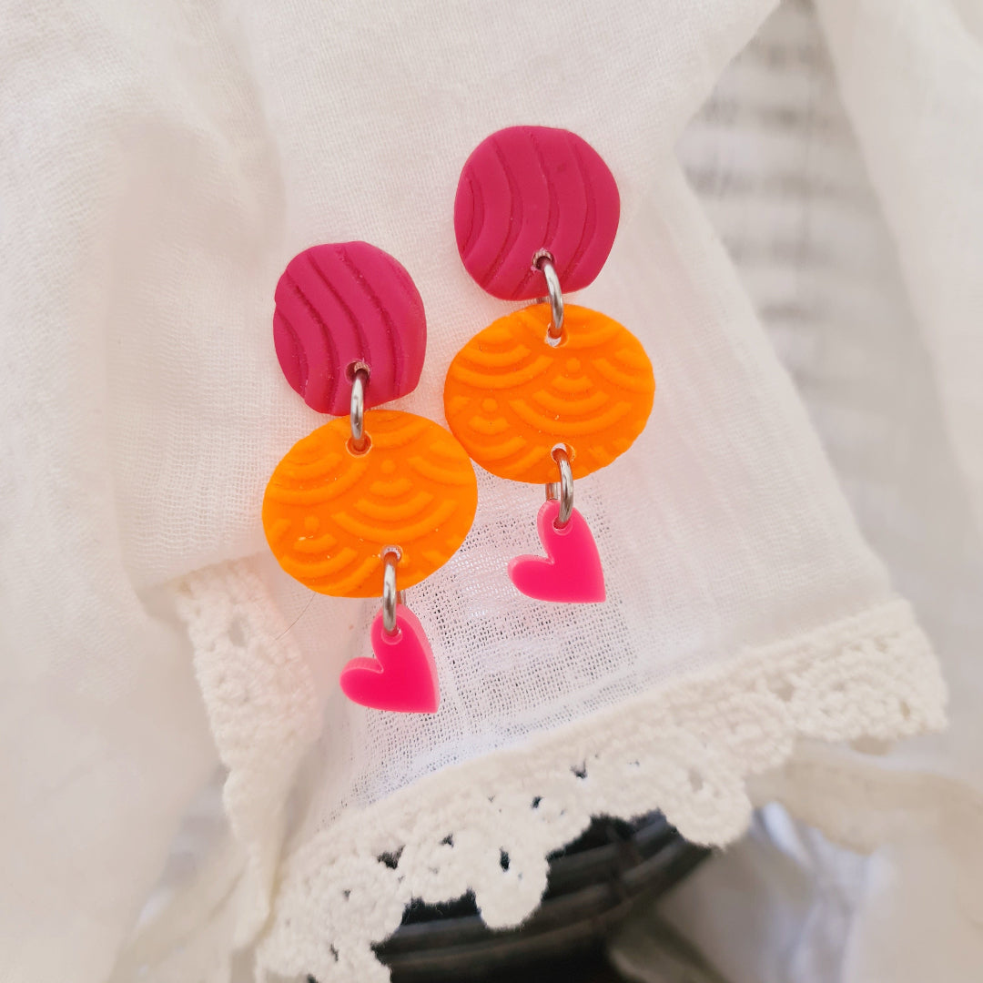Handgemaakte roze en oranje oorbellen van polymeerklei met neonroze hartje

