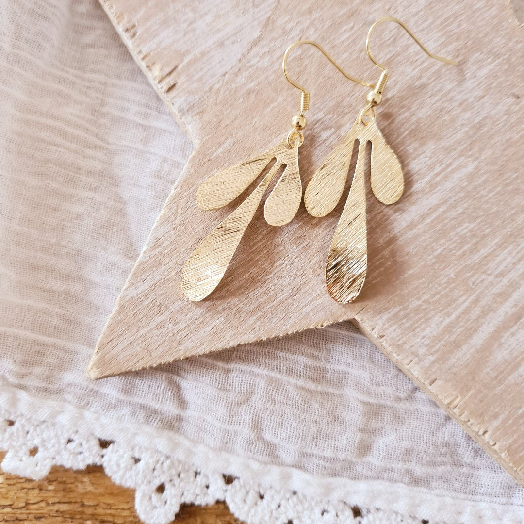 Detailfoto sierlijke gouden oorbellen met fijnmazig blad en bloemvormig design en geborstelde afwerking