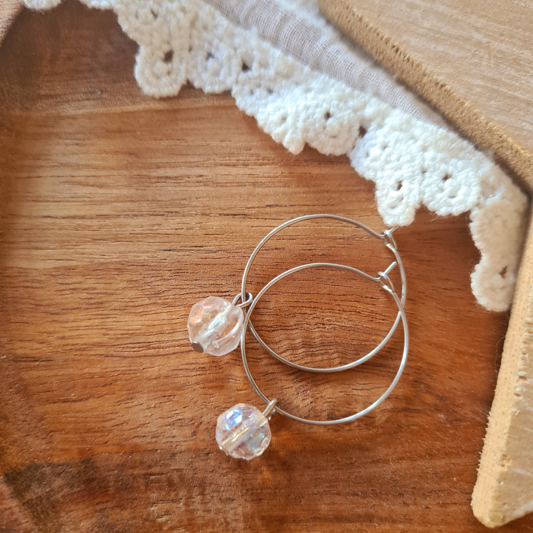 Zilveren stainless steel ringen met transparante glaskraal uit India op houten ondergrond, minimalistische oorbellen