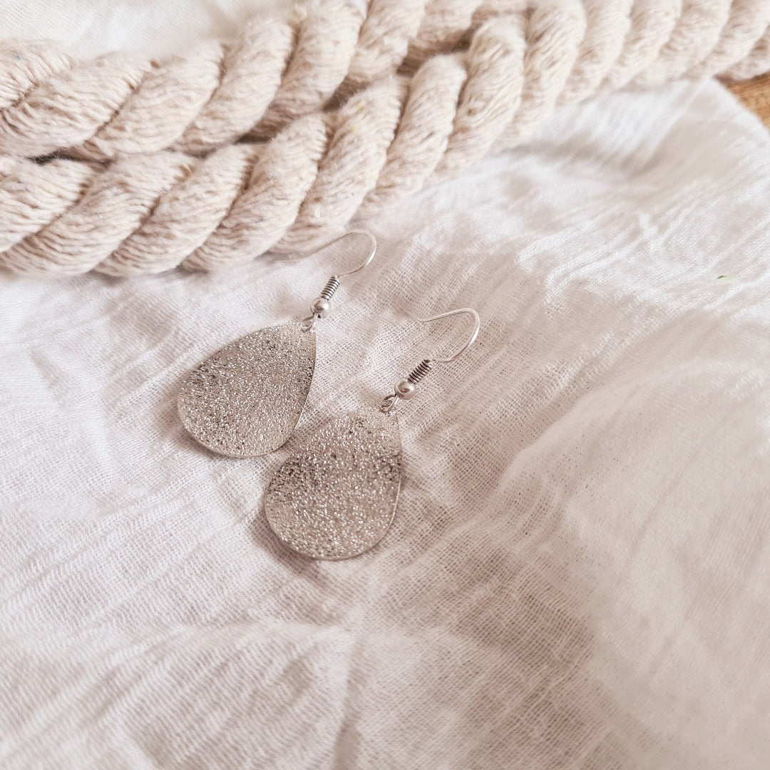 Detailfoto zilverkleurige druppeloorbellen met fijne textuur en subtiele glinstering, nikkelvrij