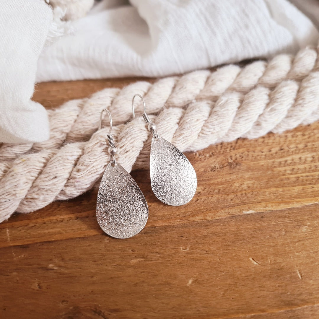 Gedragen zilverkleurige druppeloorbellen met glinstering, close-up profiel nikkelvrij stainless steel