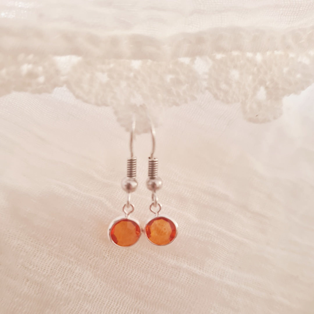 Detail zilverkleurige oorbellen met fonkelend oranje kristalglas steentje, elegante korte hangertjes